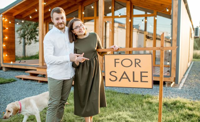 Elegant couple standing with dog near the beautiful wooden country house for sale
