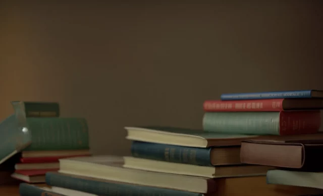 a stack of textbooks beside a piggy bank on a desk.